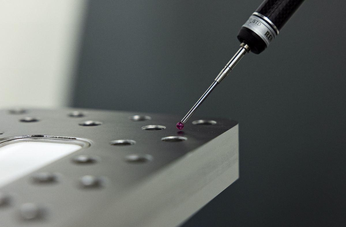 Ruby-tipped CMM probe stylus touching a hole on a precision machined plate